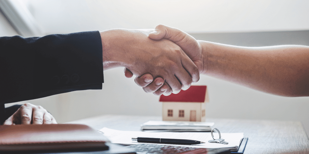 Two people shaking hands across a desk completing a real estate transaction