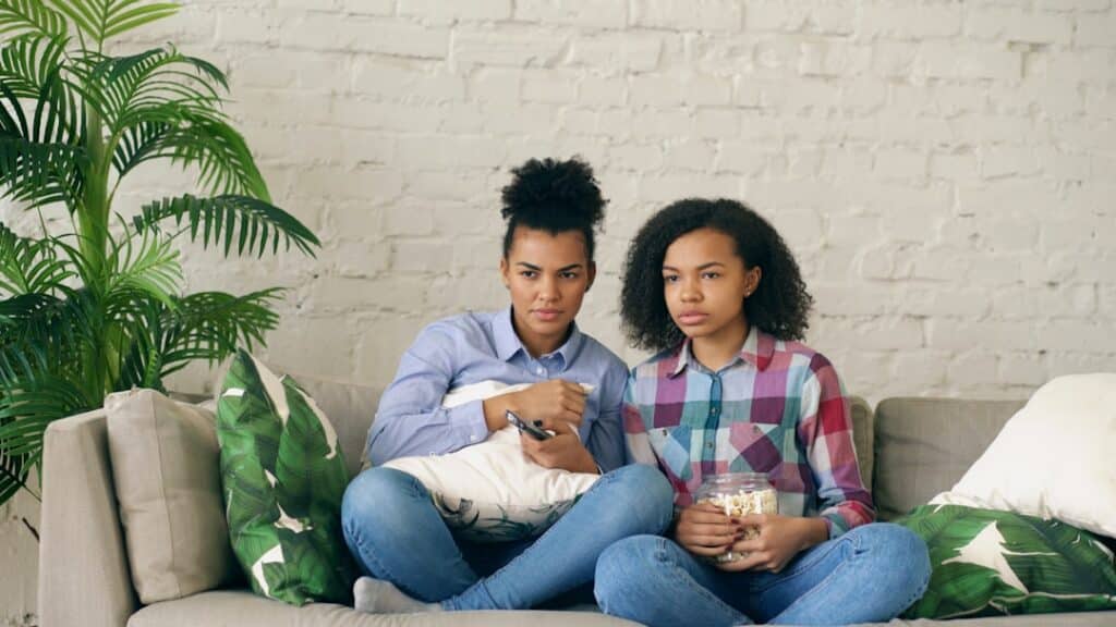 Man and a woman sit on opposite ends of a modern sofa in a well-lit living room, looking away from each other to represent...