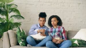 Man and a woman sit on opposite ends of a modern sofa in a well-lit living room, looking away from each other to represent...