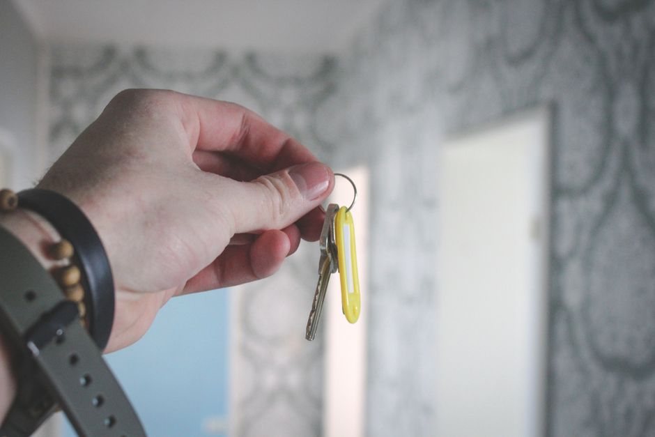 A person's hand holding a set of house keys in front of a home's front door, representing the successful completion of the property succession process.